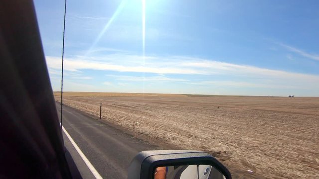 POV out of the passenger's side window while driving past harvested wheat fields in an agricultural area of Eastern Washington State; side view mirror and radio antenna visible
