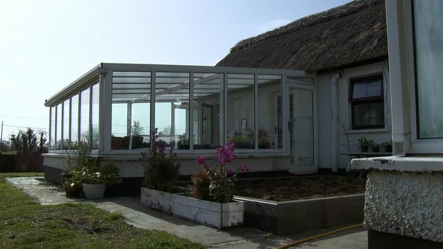 Steady, medium wide shot of a sun room attached to a home and a garden plot outside.
