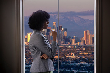 Black female businesswoman looking worried or tired by an office window with a view of downtown Los...