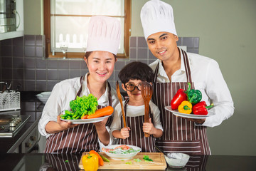  Asian woman young mother and father with son boy cooking salad food with vegetable holding tomatoes and carrots, bell peppers on plate for happy family cook food enjoyment lifestyle kitchen in home