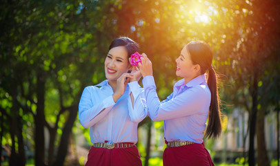 Two beautiful asian women friends in white shirt laughing and holding pink lotus flowers. Two young asian women with sarong cloth decorated with silver belt according to Thai culture, Thailand.