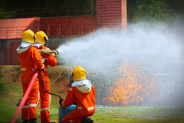 Three brave firefighter using extinguisher and water from hose for fire fighting, Firefighter spraying high pressure water to fire, Firefighters training, foreground is drop of water springer-Image
