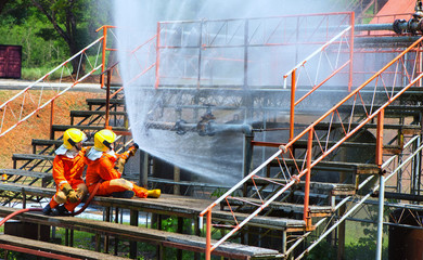 Two brave firefighter using extinguisher and water from hose for fire fighting, Firefighter spraying high pressure water to fire, Firefighters training, foreground is drop of water springer-Image
