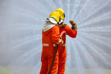 Two brave firefighter using extinguisher and water from hose for fire fighting, Firefighter spraying high pressure water to fire, Firefighters training, foreground is drop of water springer-Image