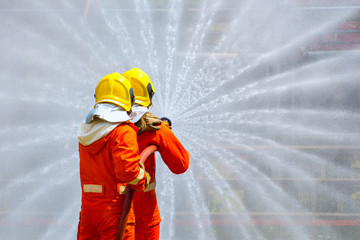 Two brave firefighter using extinguisher and water from hose for fire fighting, Firefighter spraying high pressure water to fire, Firefighters training, foreground is drop of water springer-Image