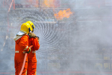 Two brave firefighter using extinguisher and water from hose for fire fighting, Firefighter spraying high pressure water to fire, Firefighters training, foreground is drop of water springer-Image