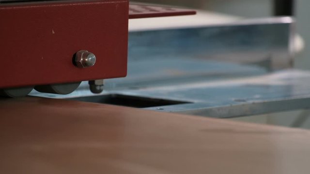 Furniture manufacture. Close-up of the machine for gluing edges on wooden parts. The beginning of the movement of the chipboard sheet on the guide rollers. The real sound of a working machine.