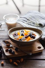 Yogurt with cherries, blueberries, pineapples, pitayas, nuts and almond milk on a brown table.