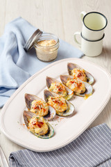 Baked mussels with cheese and bacon on white dish.