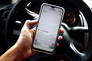 Hand holding a smartphone with a message in front of a car steering wheel