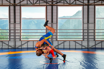 A trainer in sports wrestling tights teaches a little wrestler boy traditional throws in the style of Greco-Roman wrestling against mountains. The concept of children's sports training in martial arts