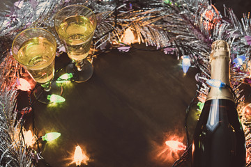 Two Glasses with champagne and bottle on a wooden table decorated with Christmas accessories to celebrate the new year and Christmas. Romantic evening. The glow from the garlands. Valentine's Day