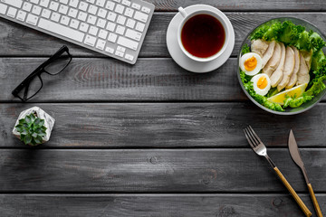 Salad bowl with healthy food on office desk with keyboard and tea on wooden background top view mock up