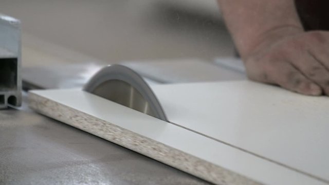 Chipboard sawing machine. A circular saw cuts off part of a white laminated wood sheet. Close-up. The real sound of a working woodworking machine.