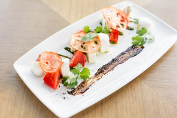 Fresh Salad with tomatoes, basil, mozzarella, and olive oil on wooden background. Italian traditional caprese salad. Mediterranean, natural and organic food concept.