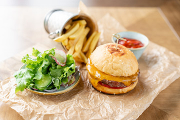 Cheeseburger with lettuce, tomato, fries, and melted cheese. The table in the restaurant. Unhealthy food.