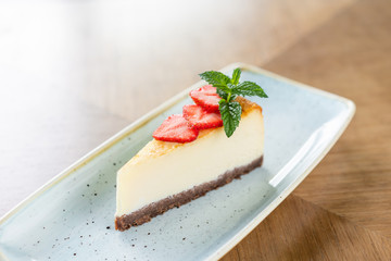 Piece of delicious cheesecake with strawberry and mint leaves on white plate.
