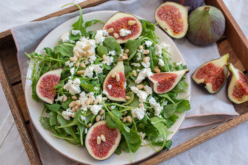 Fig salad with feta cheese, nuts and arugula on wooden background