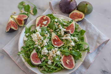 Fig salad with feta cheese, nuts and arugula on wooden background