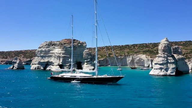 Amazing Yacht charter sailboat in Kleftiko bay Milos greece.  Popular white sea arch and rock formations in the backdrop.  Simple aerial forward pan.