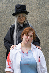 Two disguised young women, one in black with a hat and a blood smeared with a white coat