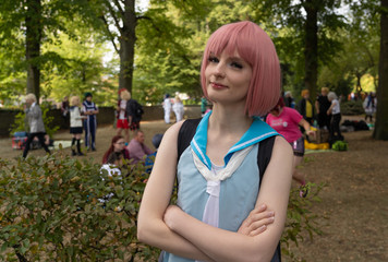 Young woman with pink hair and blue dress in a park with many not recognizable people in the background