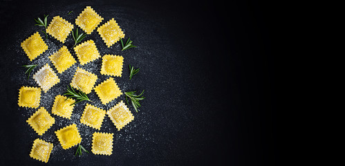 Ravioli with flour and herbs on black  background. Italian ravioli making process. Top view, copyspace