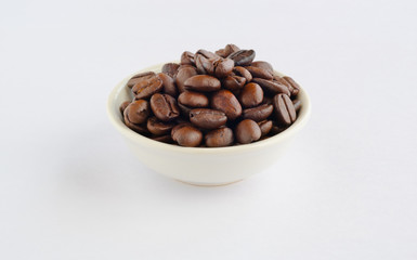 Roasted coffee beans in bowl on white background