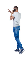 Naklejka premium Back view of pointing man in jeans walking with a mobile phone.