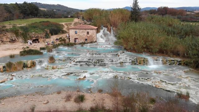 In Saturnia Italy, the drone flies towards the hot spring baths and then rises up and follows the trail of where all the water originates.