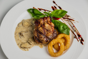 A top view horizontal photo of a steak with onion rings and mushroom sauce, basil, white plate.