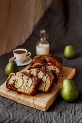 A seasonal cake with pears served on a wooden cutting board, fresh pears, coffee with milk in a white cup, milk in a bottle. Natural light. Vertical.