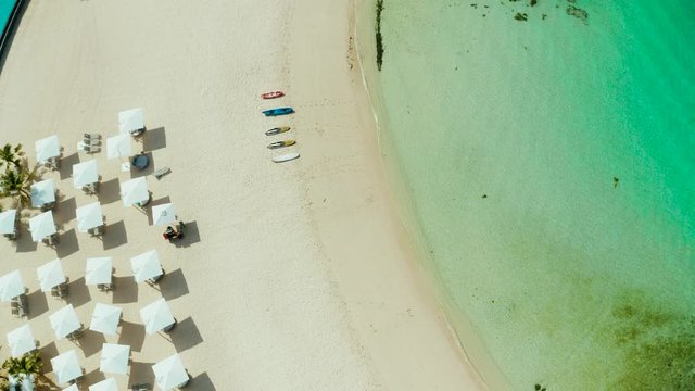 Beach umbrellas and deck chairs on the white beach. White sandy beach and clear turquoise lagoon, top view.