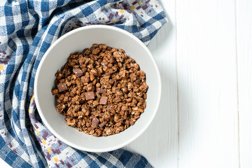 Top view on fresh chocolate granola in grey bowl with blue cloth on white wooden background. Copy space. Healthy and tasty breakfast. Vegan food. Food photo background