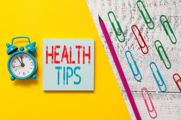 Handwriting text Health Tips. Conceptual photo advice or information given to be helpful in being healthy Notepad marker pen colored paper sheet clips alarm clock wooden background