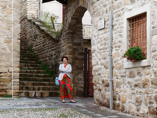 beautiful woman in a red dress stands at the stone wall of the old city