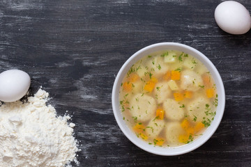 Top view of soup in bowl with dumplings on black background