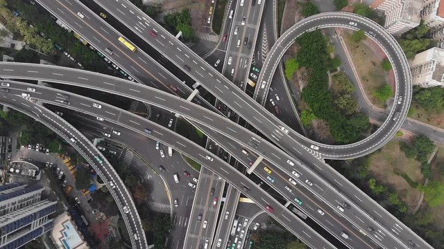 Large inner-city roads interchange at Guangzhou, aerial camera look straight down from height. Modern transportation network at Chinese megalopolis, vehicles move on all levels of stacked junction