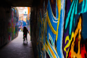 Fototapeta na wymiar Close up of a blue and yellow graffity in Werregarenstraat (Graffiti Street) in Ghent, Belgium, Europe, with defocused background with a person on a bike. Colorful famous street in the old town