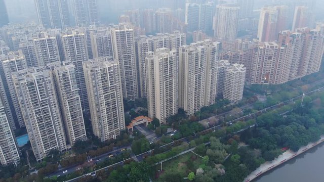 Modern mansion unit in Chinese city, aerial shot in evening mist. Modern real estate at Tianhe District of Guangzhou, green park at Pearl River embankment seen downwards