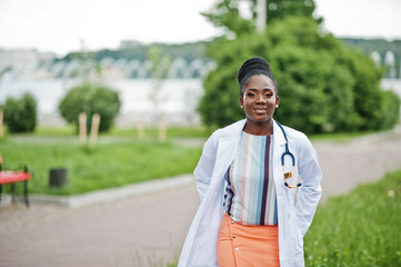 Young african american female doctor in white coat with a stethoscope posed outdoor.