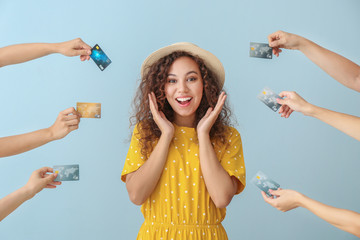 Young African-American woman and hands with credit cards on color background