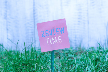 Writing note showing Review Time. Business concept for to think or talk about something again Set schedule to review Plain paper attached to stick and placed in the grassy land