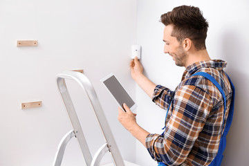 Electrician with tablet computer installing alarm system indoors