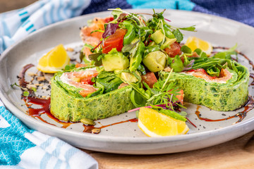 A serving of Salmon Roulade on a white plate, surrounded by sauce and lemon wedges