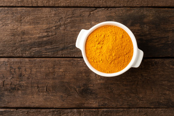 Turmeric powder in bowl on retro wooden background. Top view