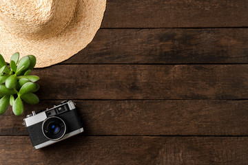Photo camera with straw hat and small flower on wooden table. Travel background concept