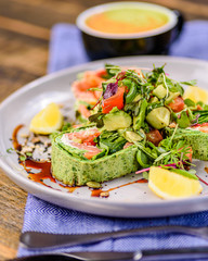 A serving of Salmon Roulade on a white plate, surrounded by sauce and lemon wedges