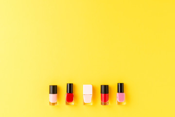 Red and pink nail polishes on yellow background with copyspace. Top view