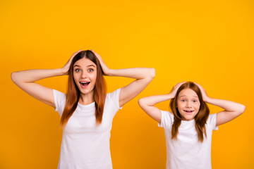 Fototapeta na wymiar Portrait of impressed mom with her daughter having long haircut touching their head screaming wow omg isolated over yellow background